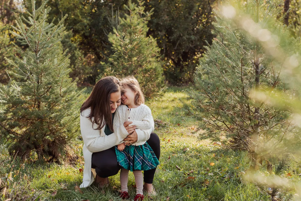 Family of four sitting on a blanket among evergreens at a Christmas tree farm