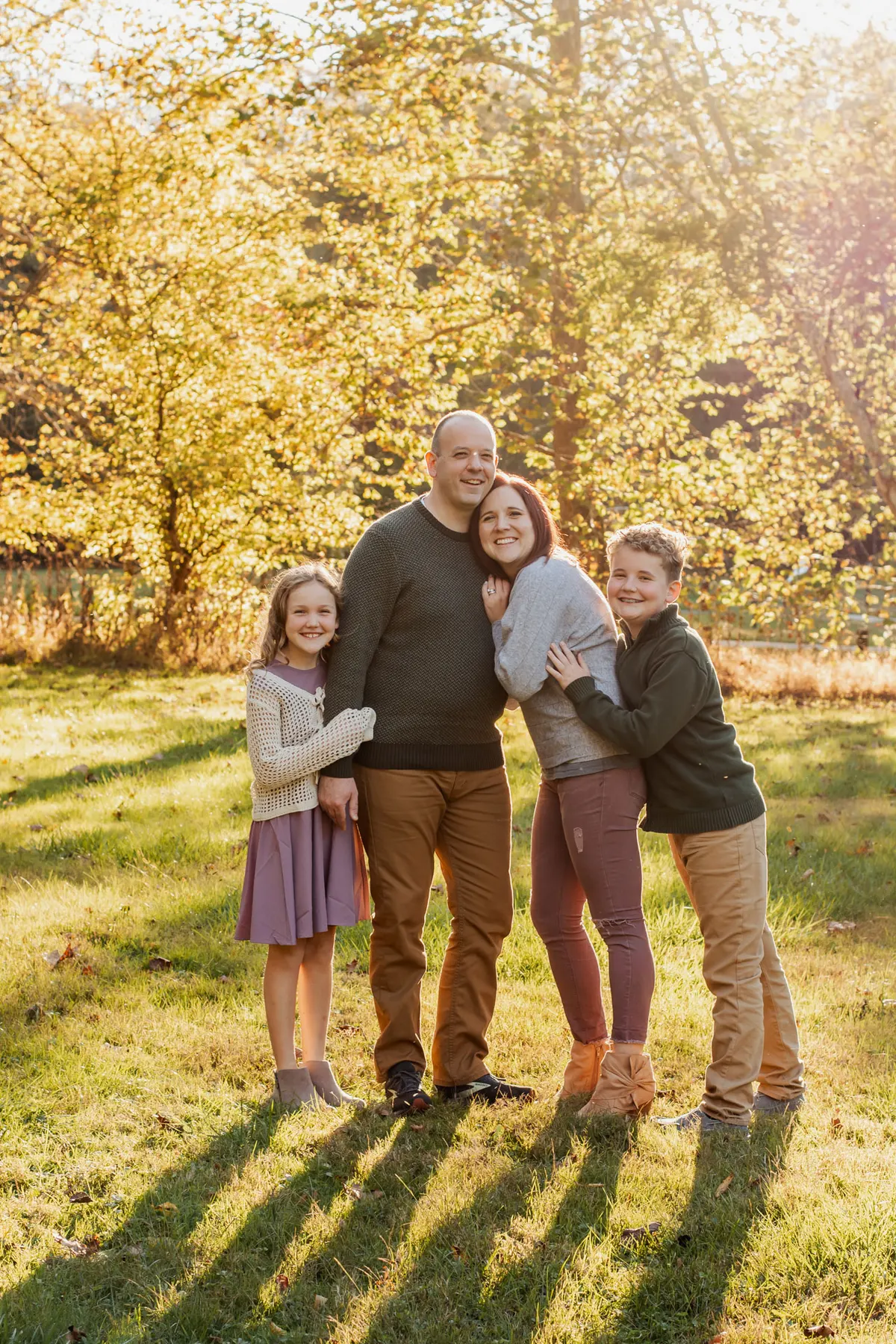 Family of four hugging in a sunlit clearing in fall