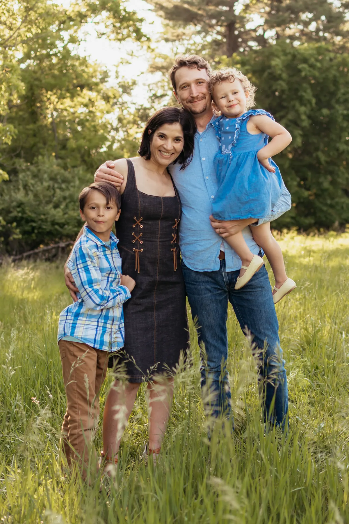 Family of four standing in tall grass in warm evening light