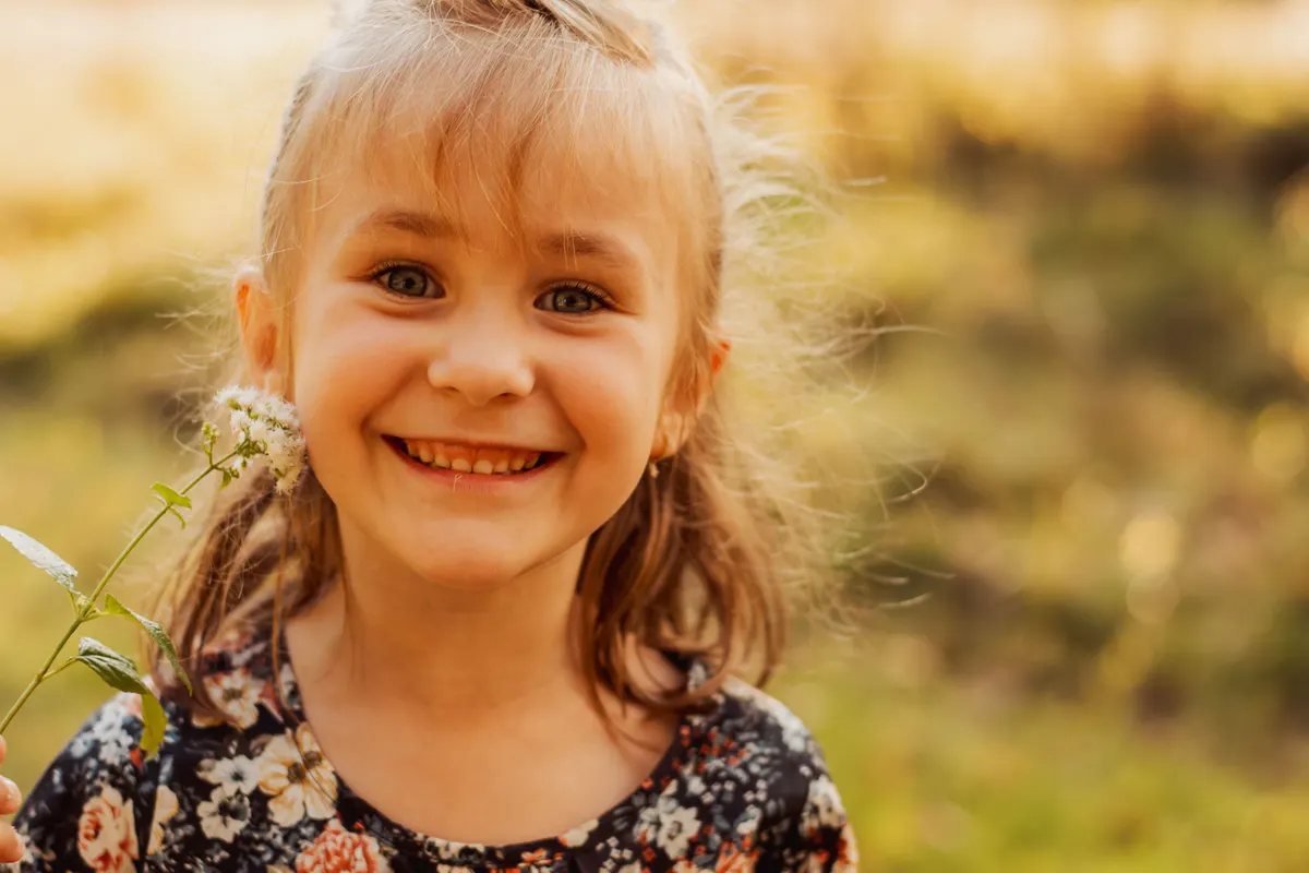 Close-up of a smiling girl in a field at golden hour