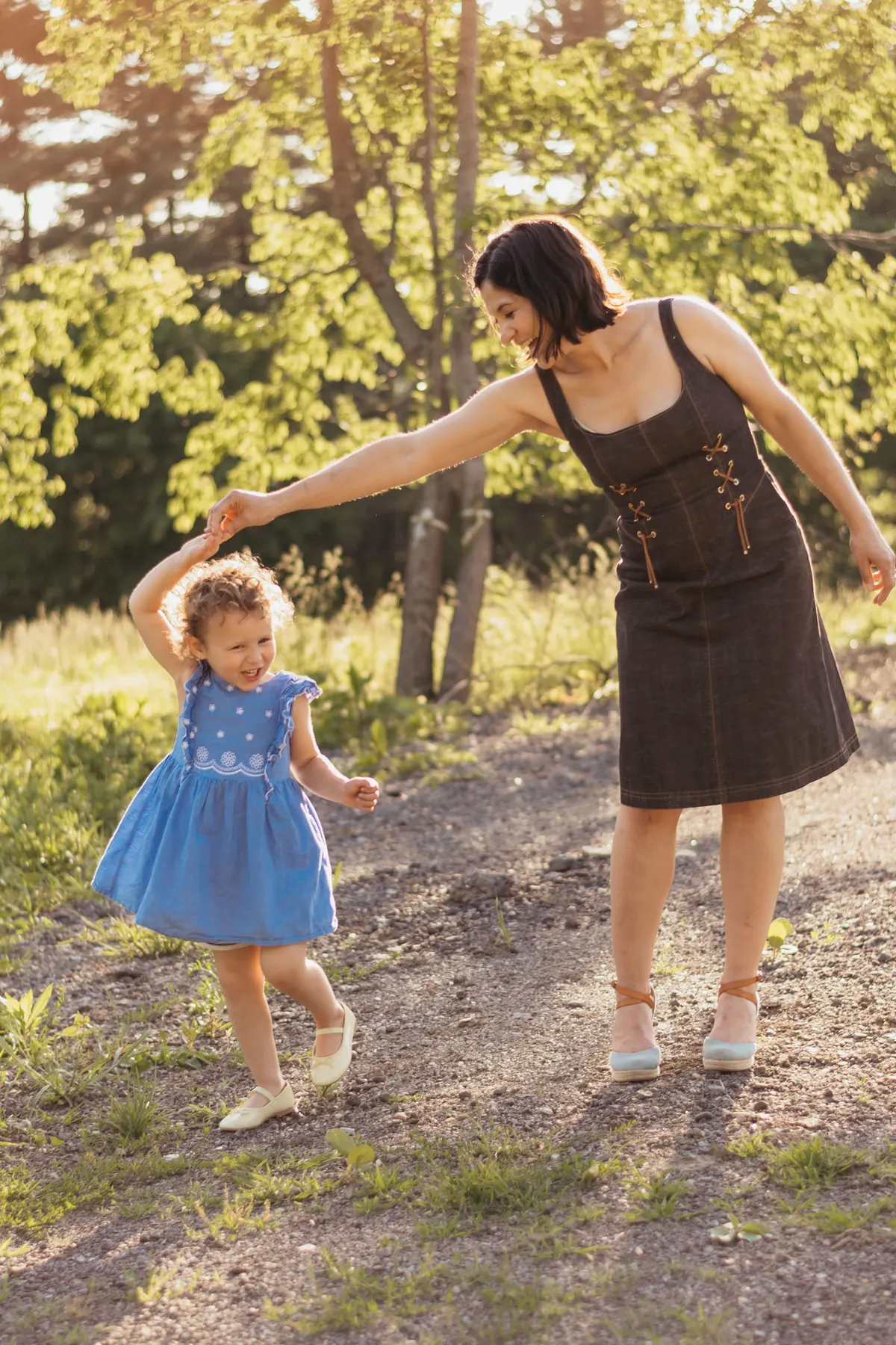 Mother spinning her toddler daughter on a sunlit path