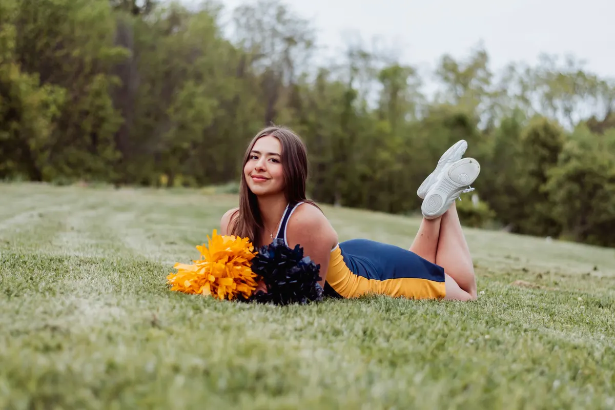Mt. Lebanon senior in her cheer uniform lying in the grass with pom-poms