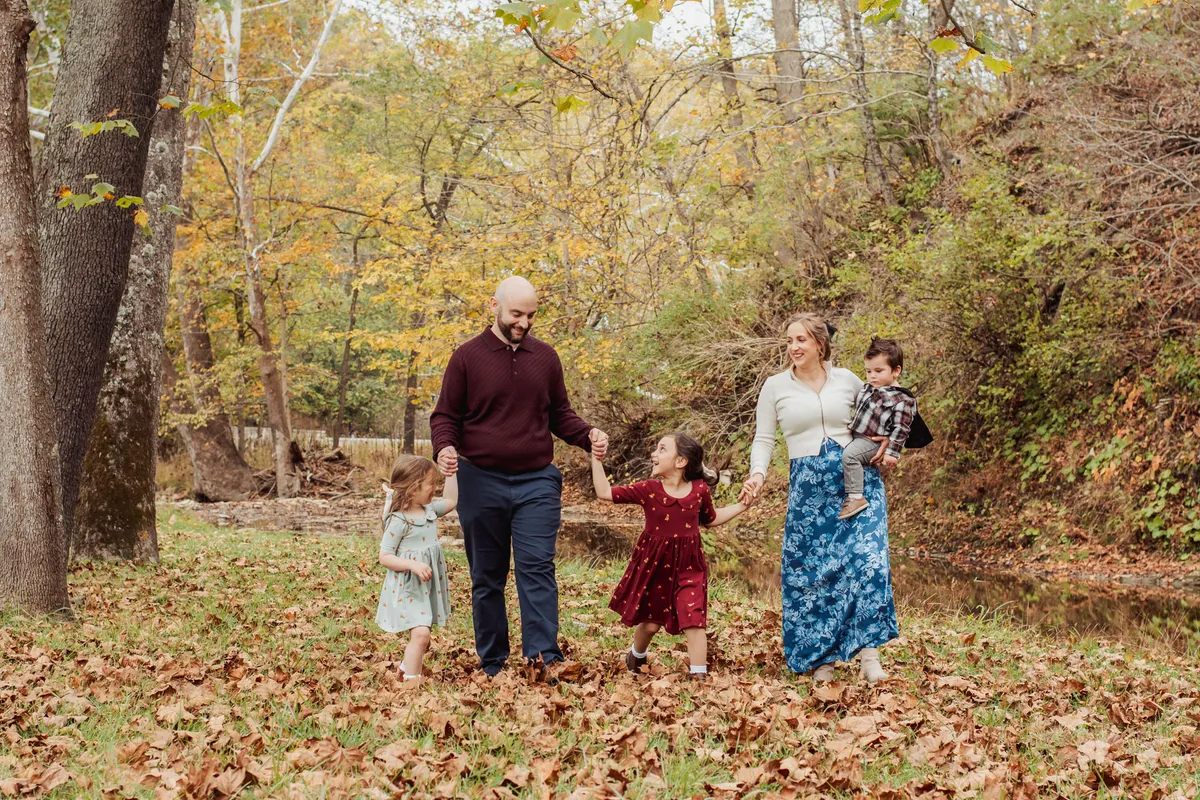 Family walking hand in hand through fall leaves in a wooded park