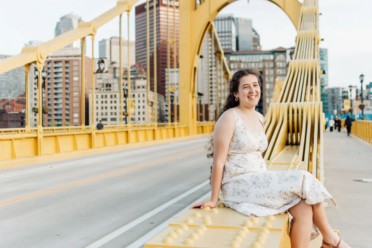 Senior sitting on the Roberto Clemente Bridge with the downtown Pittsburgh skyline behind her